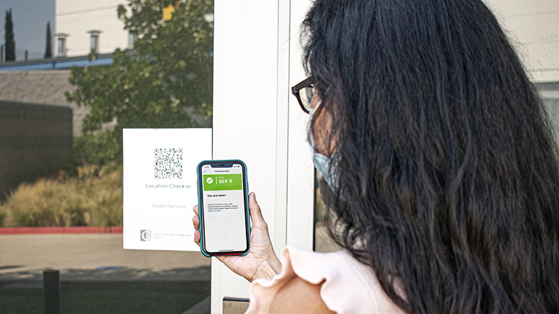 a staff member wearing a face mask scans the QR code posted on the door of a campus building